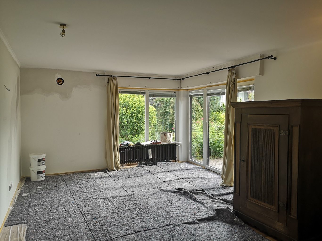 Immobilie Münster Heller Wohnraum mit großen Fenstern, grauem Teppich und Holzschrank.