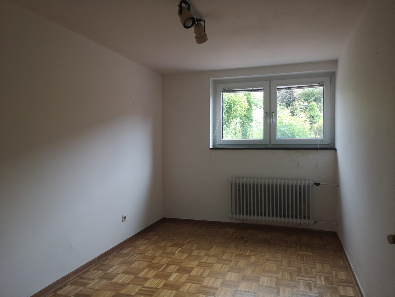 Beratung Immobilie Leerer Raum mit Fenster, Heizkörper und Parkettboden.