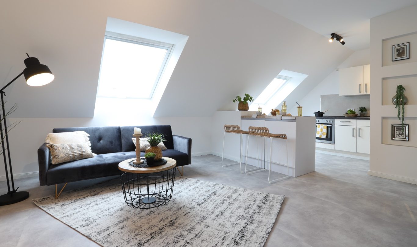 Immobilienmakler Münster Moderne Wohnküche mit Sofa, Tisch und Pflanzen in einem hellen, offenen Raum.