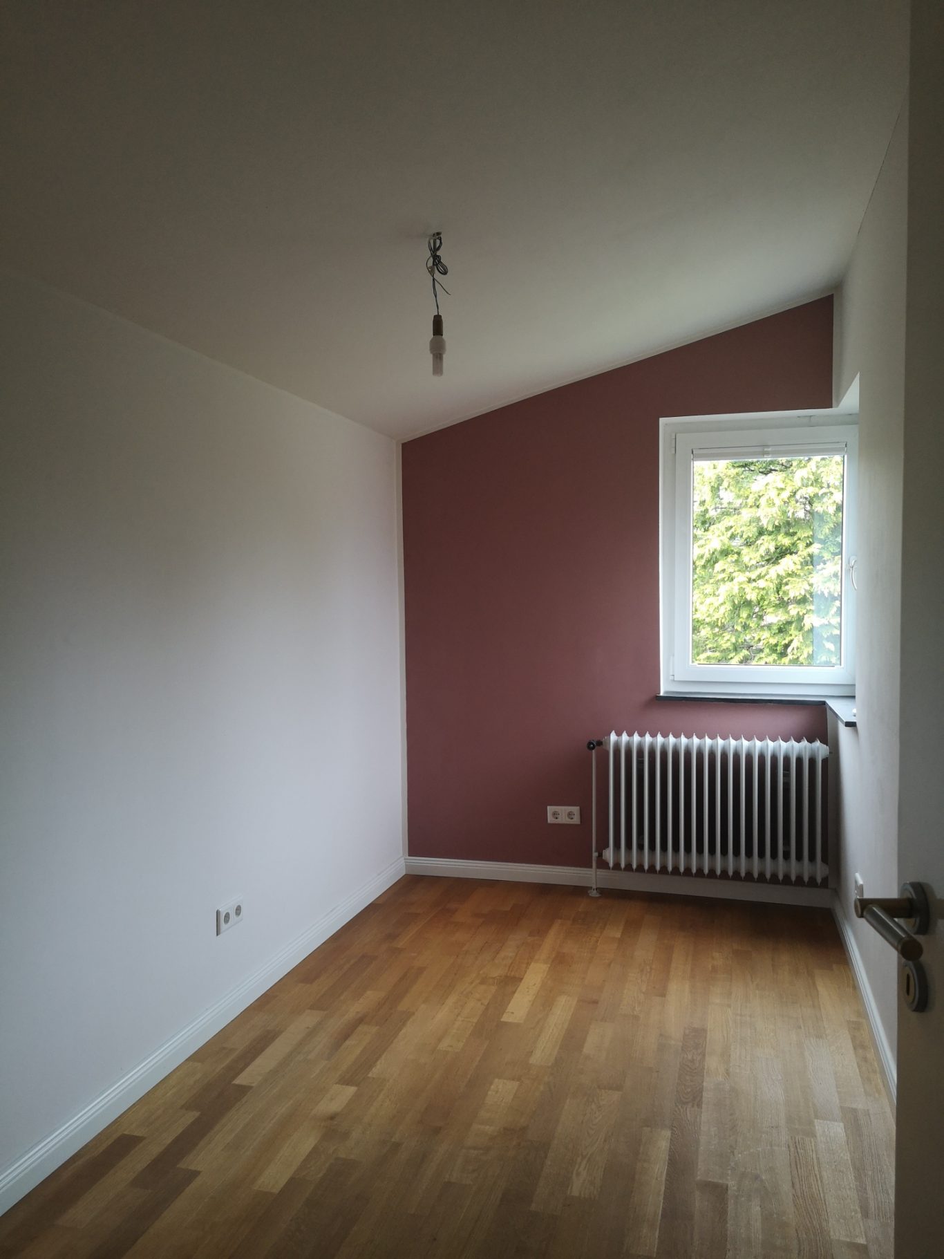 Kostenlose Videowerbung Leerer Raum mit schräger Decke, roter Wand und Fenster mit Blick ins Freie.