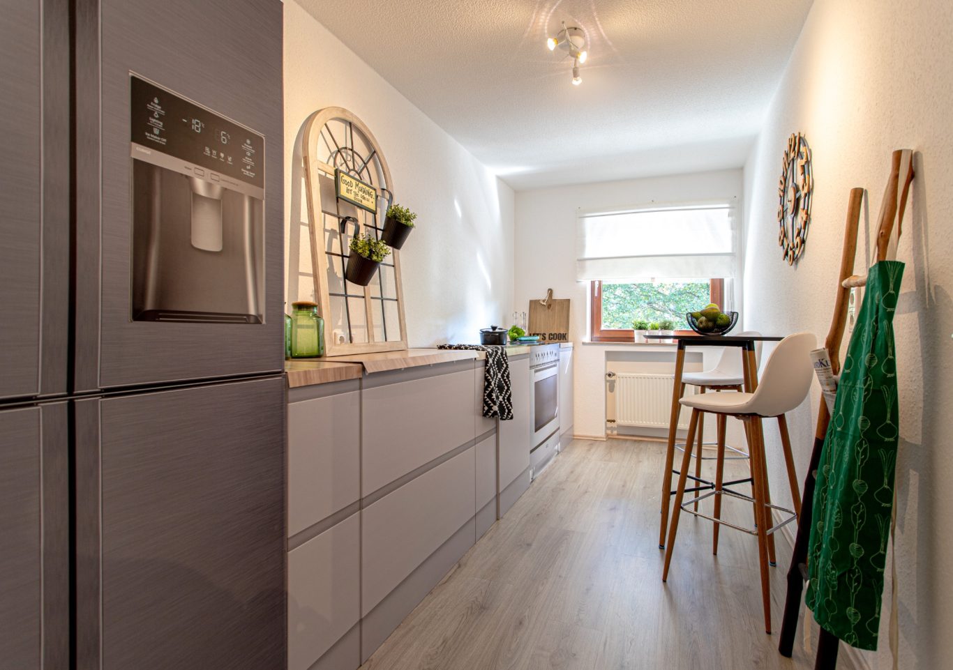 Immobilienmakler Münster Moderne Küche mit Holz-Elementen, Kühlschrank, Stuhl und Pflanzen.