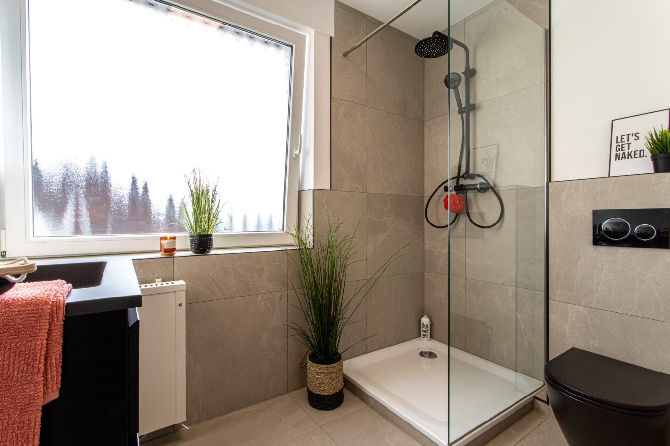 Immobilienmakler Münster Helle und moderne Dusche mit Pflanzen, Handtüchern und minimalistischer Einrichtung.