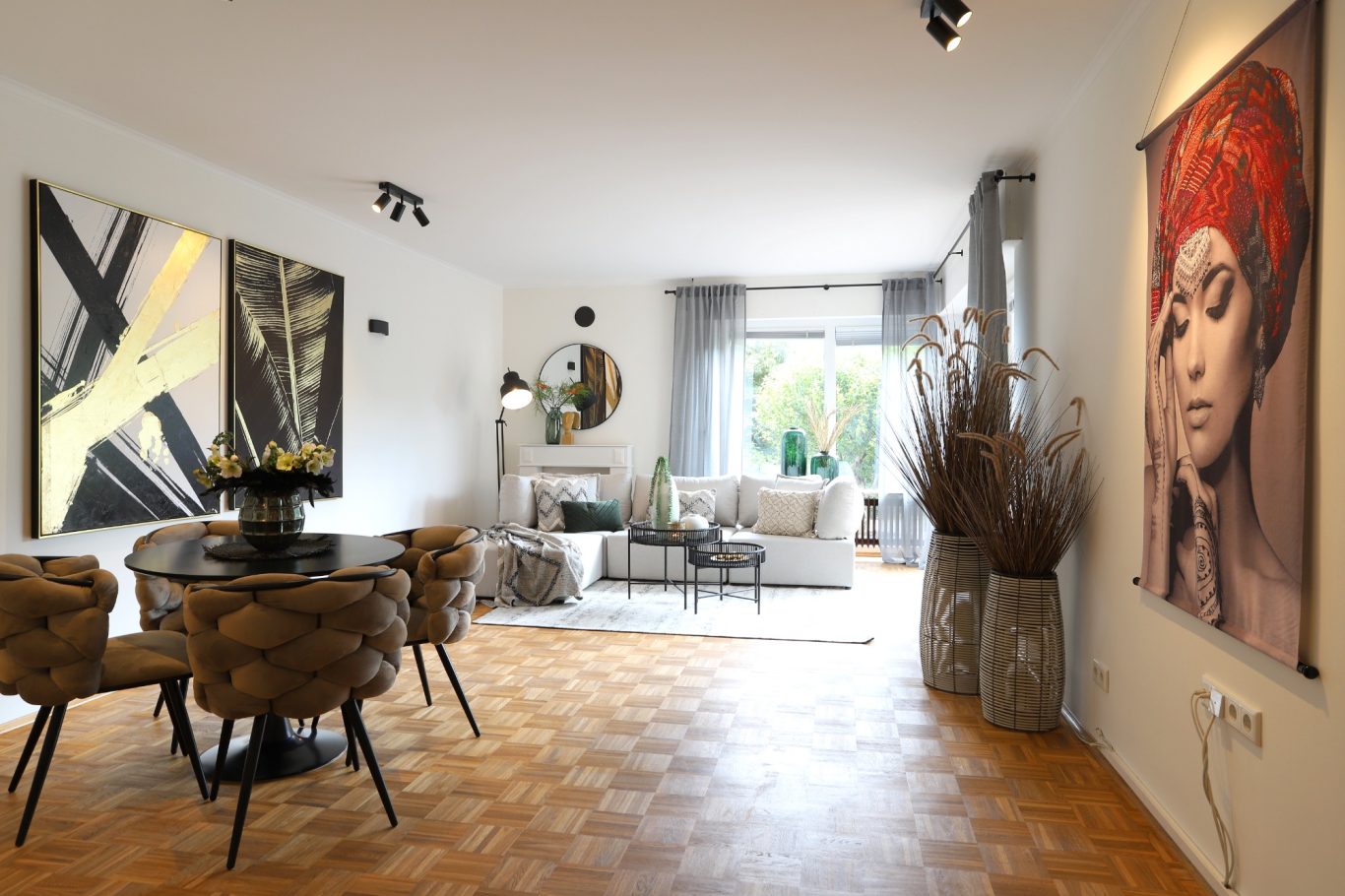 Immobilienmakler Münster Modernes Wohnzimmer mit Tisch, Stühlen, Kunstwerken an den Wänden und viel Licht.