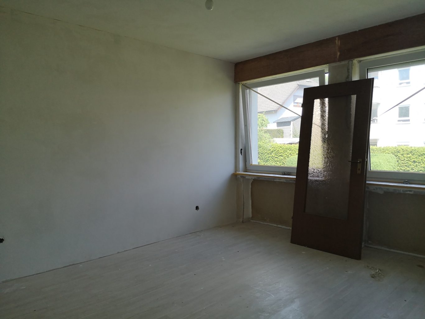 Immobilienmakler Münster Leerer Raum mit großen Fenstern und einer offenen Tür im Hintergrund.