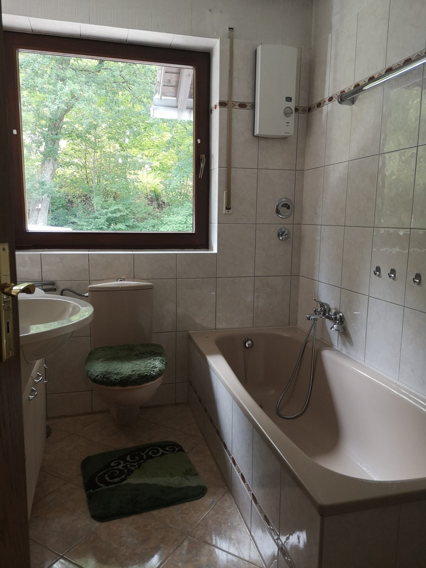 Immobilienmakler Münster Badezimmer mit Toilette, Badewanne und Waschbecken, Fenster mit Blick ins Grüne.