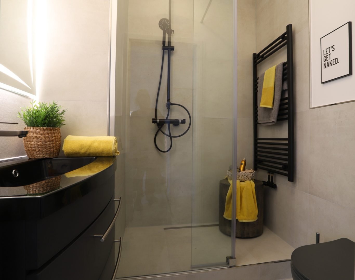 Immobilienmakler Münster Moderne Badezimmer mit Dusche, schwarzem Waschbecken und gelben Handtüchern.