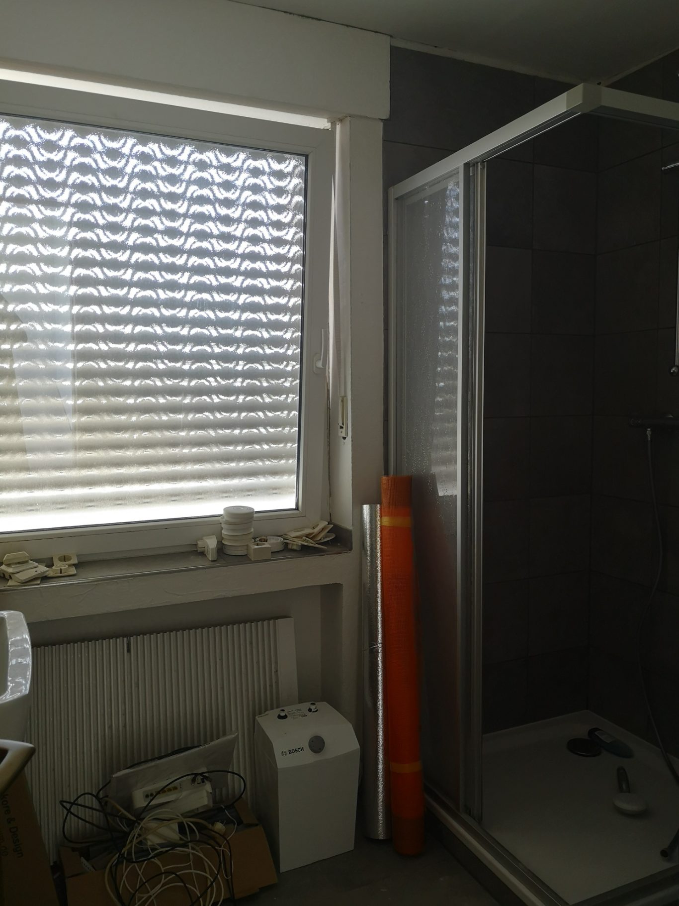 Immobilienmakler Münster Badezimmer mit Dusche, Fenster mit Jalousien und orangefarbigem Rohr im Hintergrund.