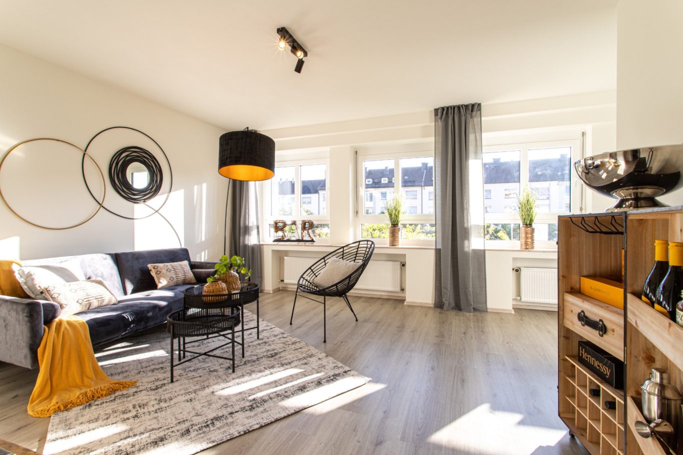 Immobilienmakler Münster Helles Wohnzimmer mit Sofa, Sesseln, Pflanzen und großen Fenstern. Modernes, gemütliches Ambiente.