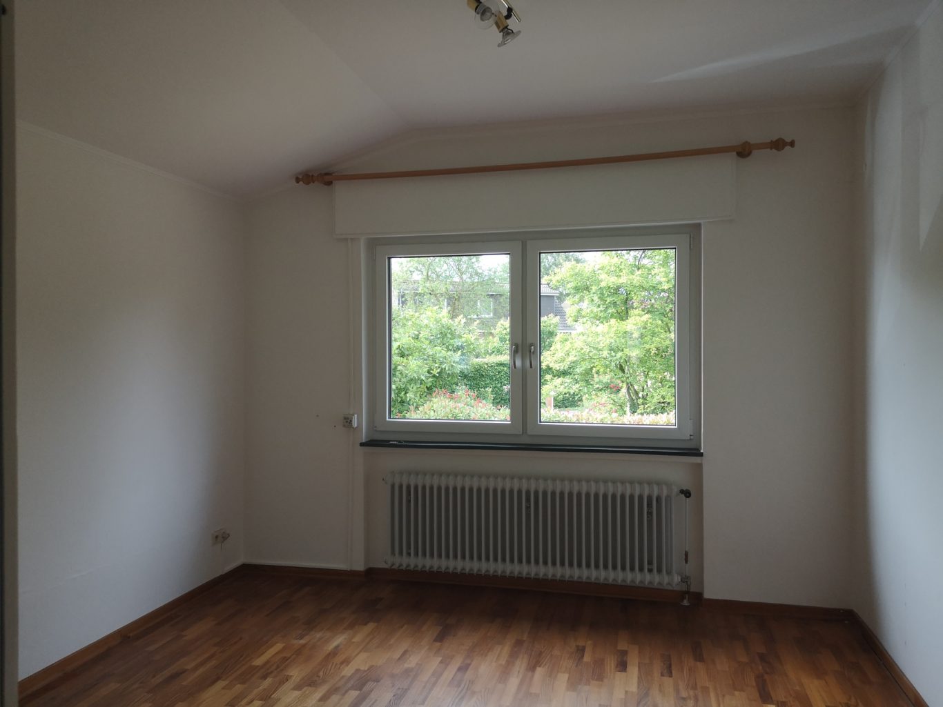 Wohnung Münster Leerer Raum mit Fenster und Blick auf einen grünen Außenbereich. Holzboden.
