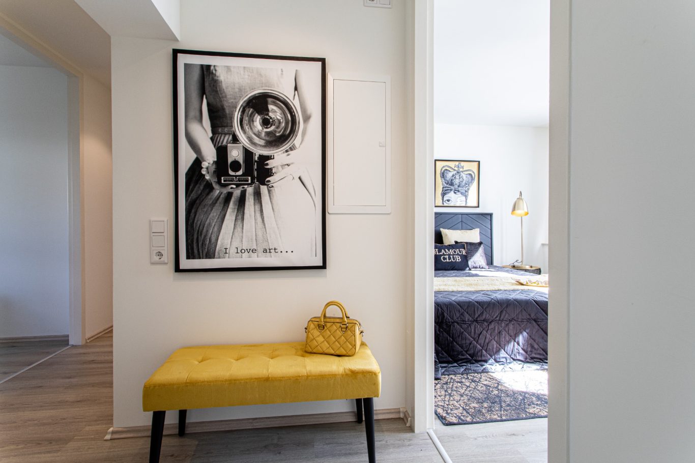 Haus verkaufen Münster Schmaler Flur mit gelber Bank, Kunstwerk an der Wand und Blick zur Schlafzimmer-Ecke.