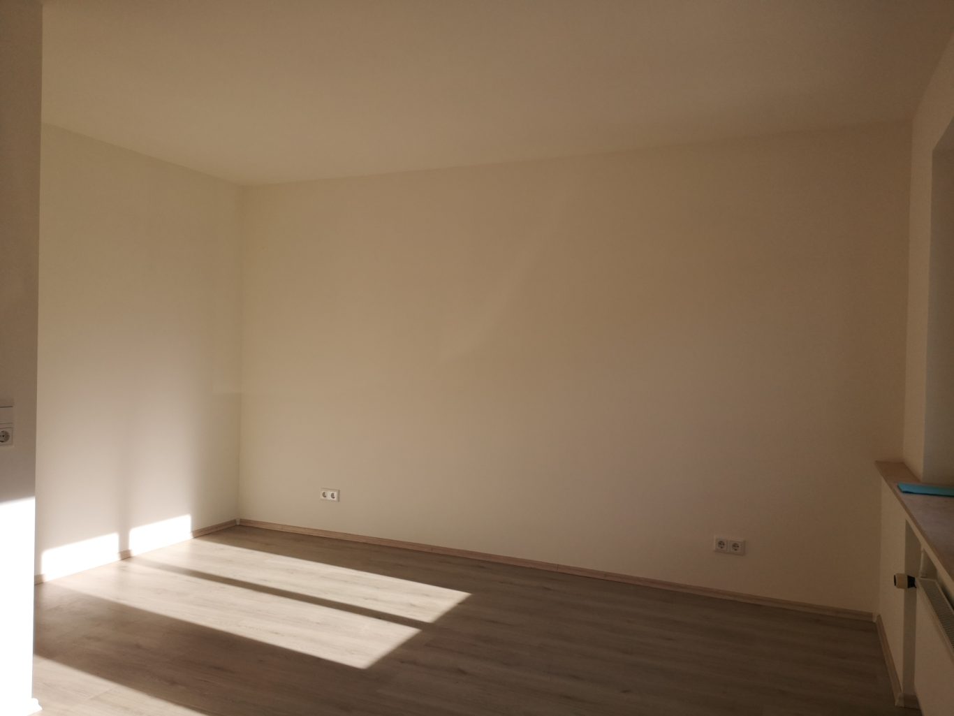 Immobilienmakler Münster Heller, leerer Raum mit Holzfußboden und Lichtstrahlen auf der Wand.