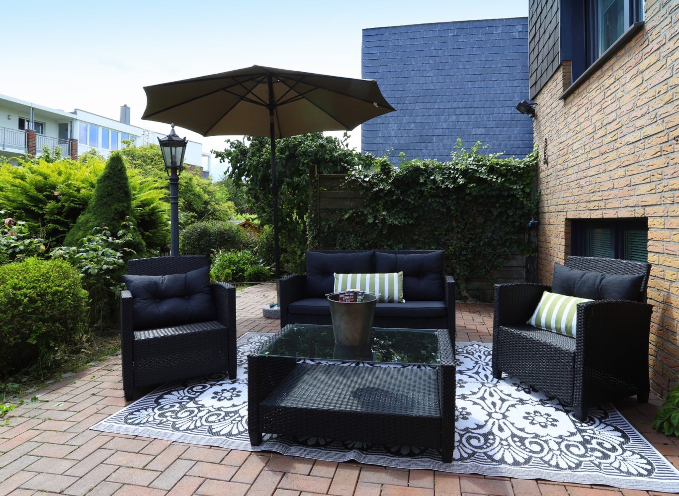 Immobilien mit Garten Sitzgruppe mit schwarzen Möbeln und Sonnenschirm auf einem gepflasterten Innenhof.