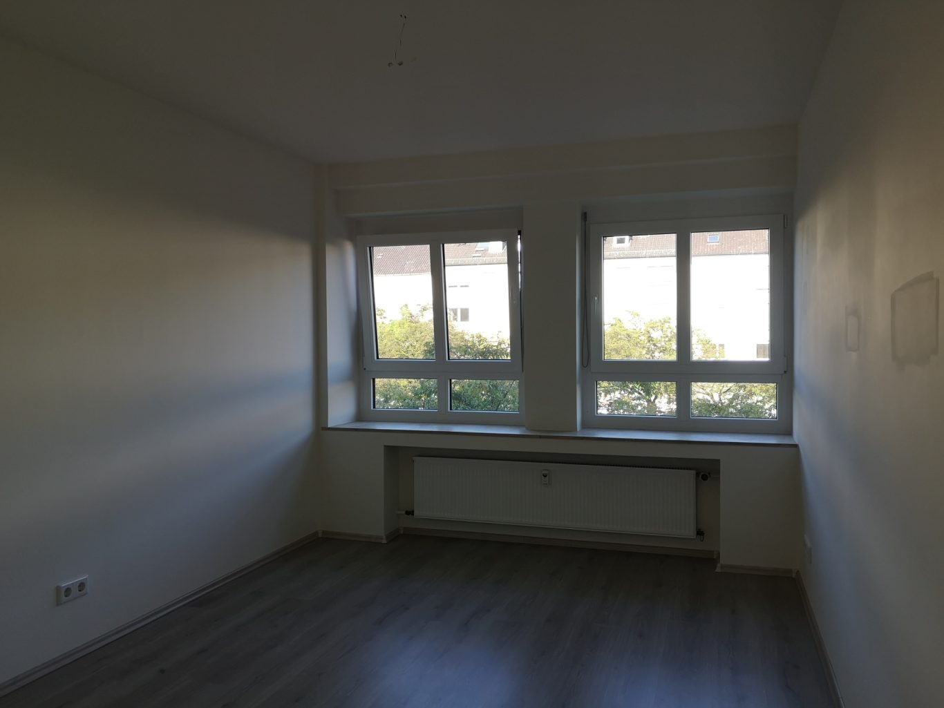 Immobilienmakler Münster Helle, leere Ecke eines Raumes mit zwei Fenstern und einem Heizkörper.