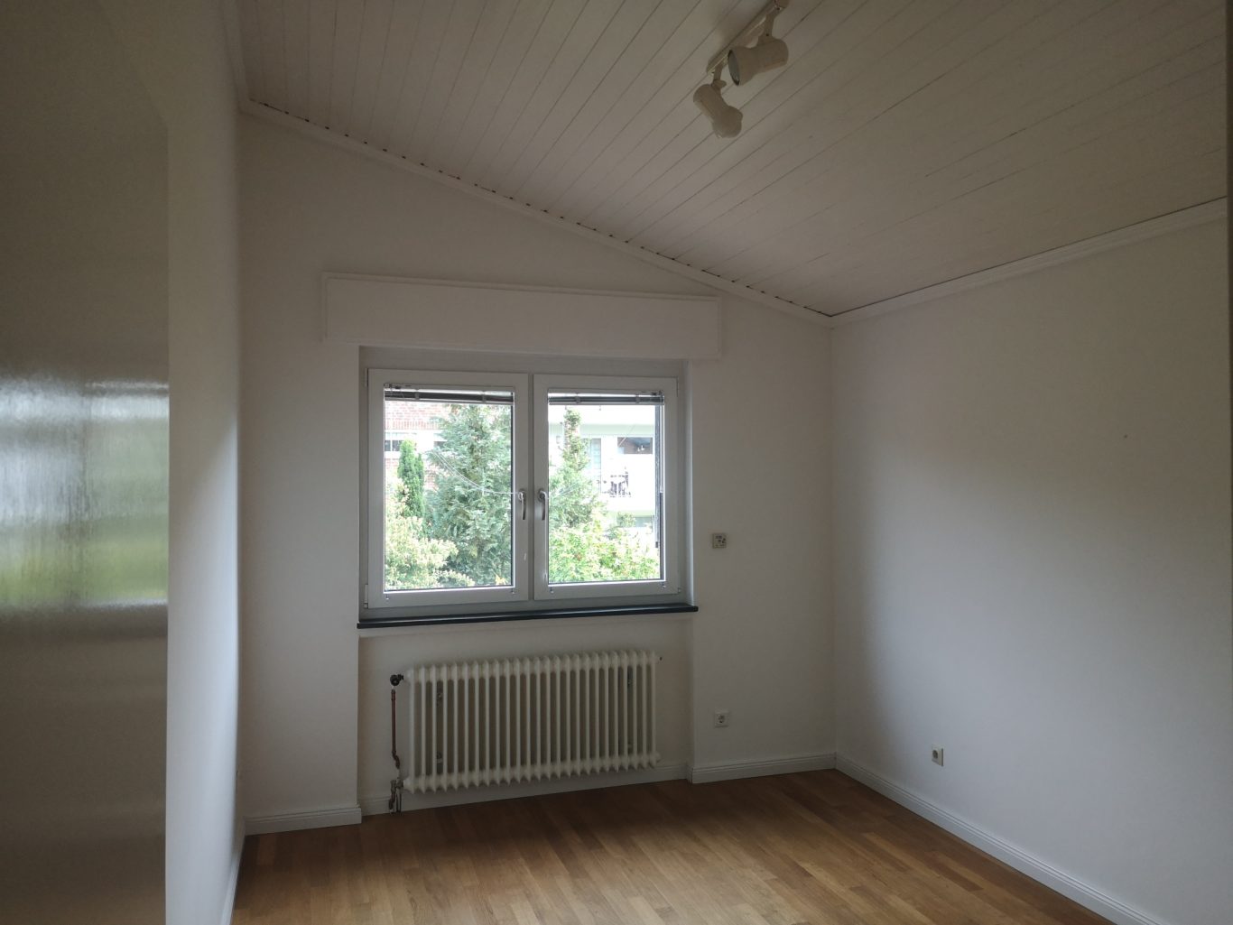 Renovierung Haus Helles, leeres Zimmer mit Holzfußboden und zwei Fenstern auf eine grüne Aussicht.