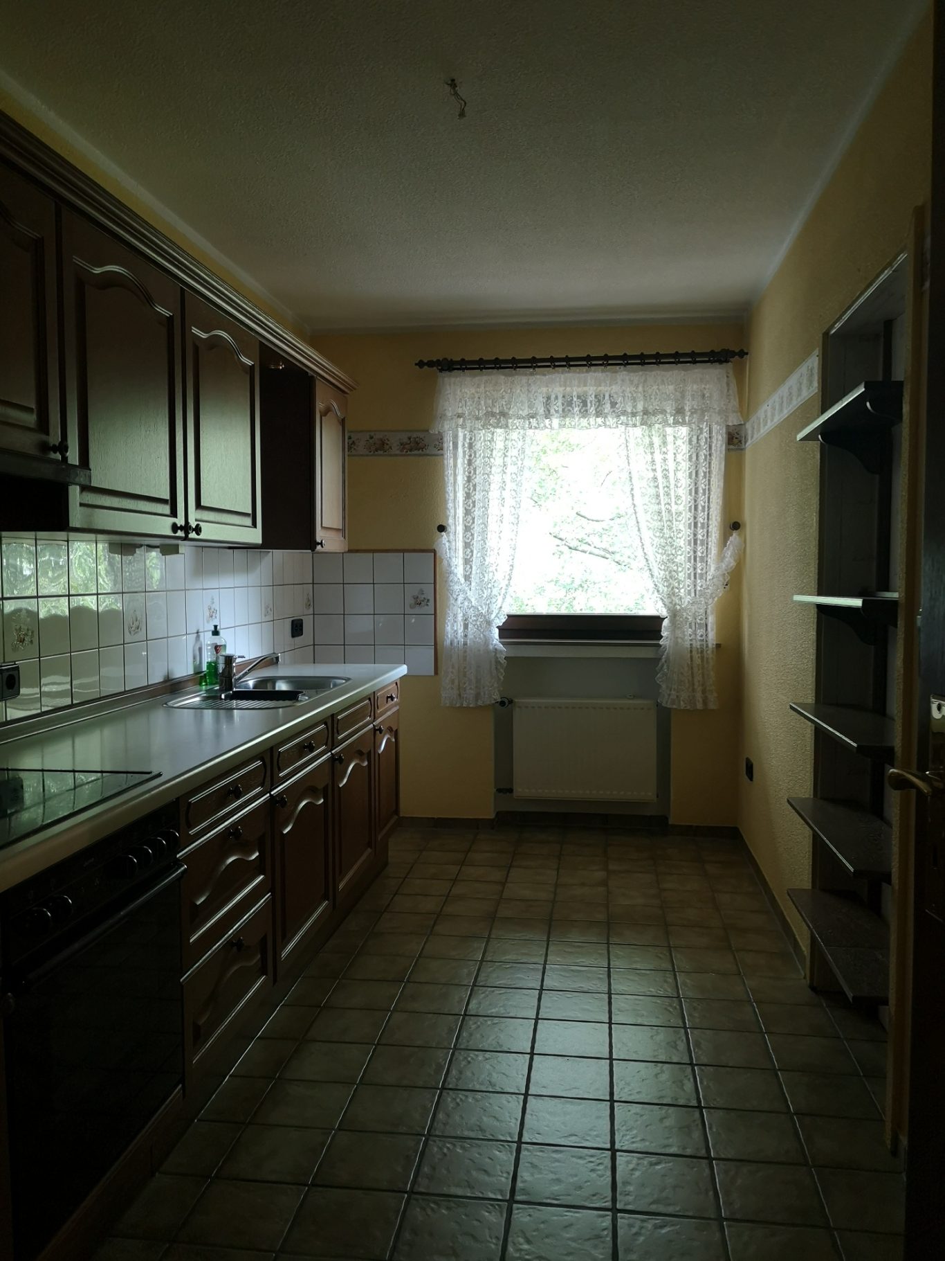 Immobilienmakler Münster Helle Küche mit Holzschränken, Fenster und Fliesenboden.