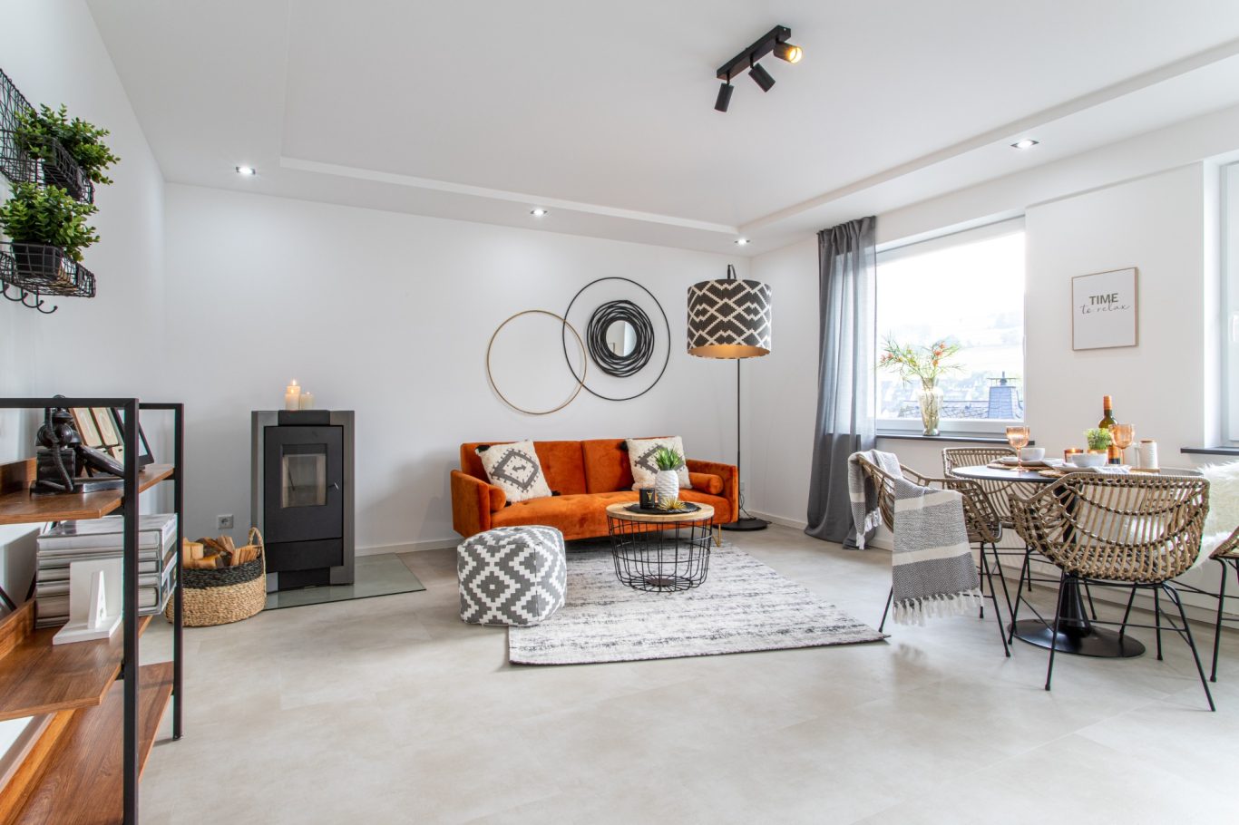 Immobilienmakler Münster Modernes Wohnzimmer mit oranger Couch, runder Wanddekoration und Essbereich.